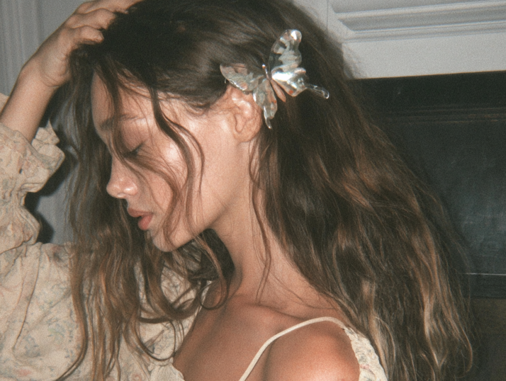 Close-up profile portrait of woman with wavy hair wearing silver butterfly hair clip, soft vintage lighting, boho style.