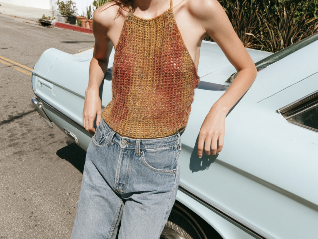 Person leaning on vintage blue car in crochet halter top and high-waisted jeans, summer street style fashion