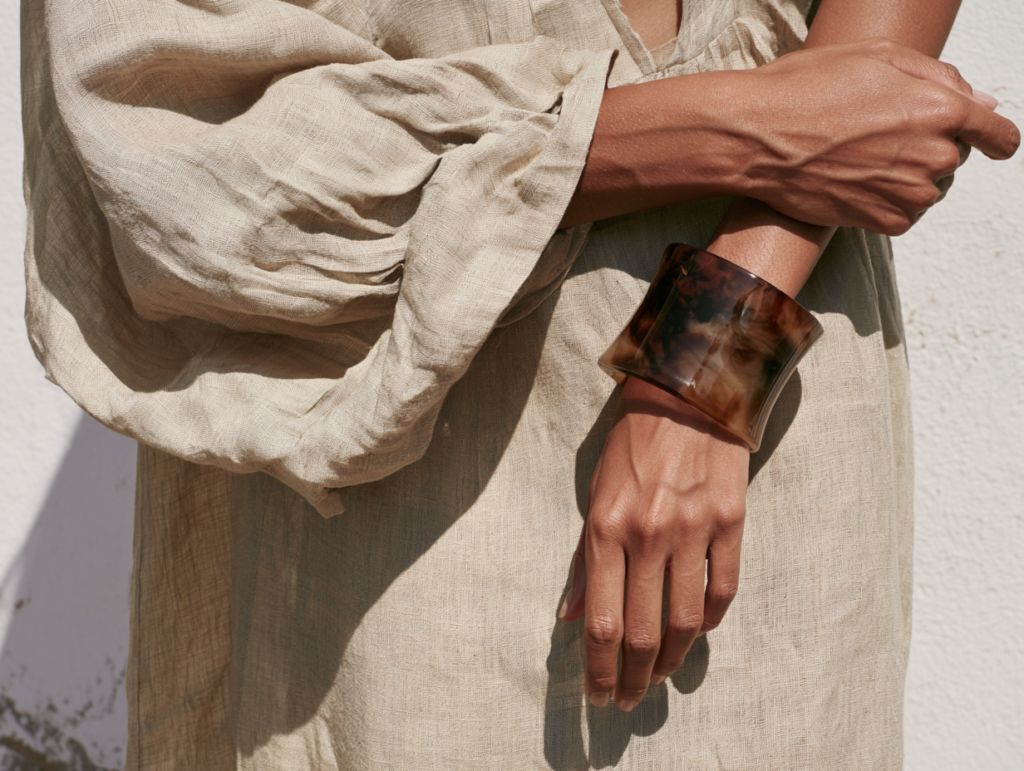 Close-up of person in beige linen dress wearing a wide marbled resin cuff bracelet, minimalist summer fashion.