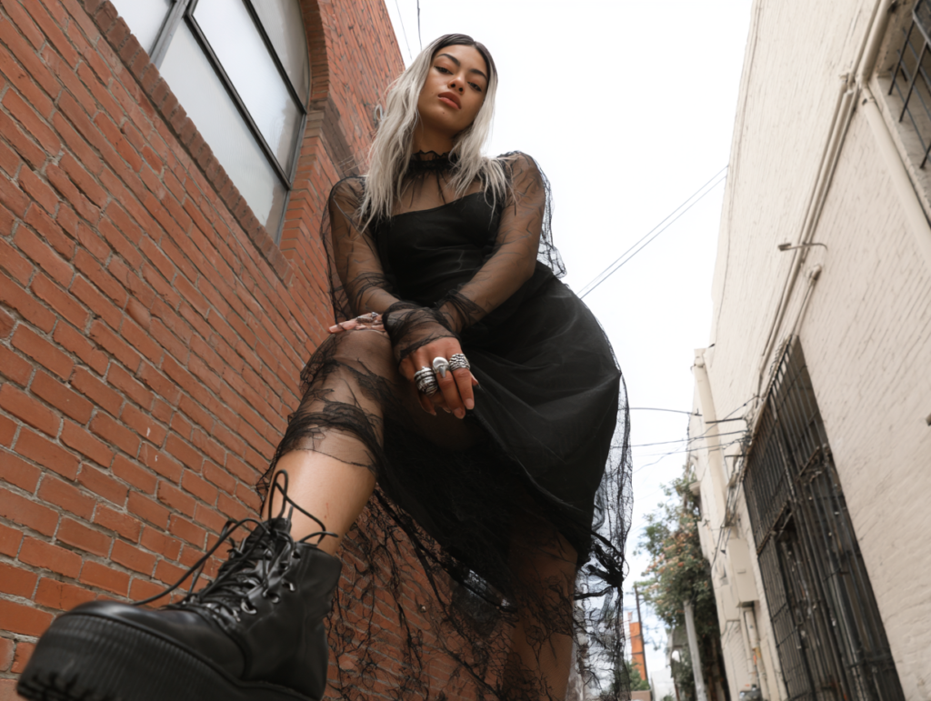 Edgy street style: person in black lace dress and platform combat boots posing in urban alley, low-angle photo with rings.
