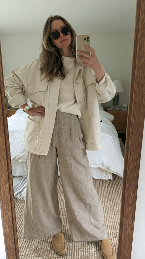 Minimalist neutral outfit mirror selfie: oversized beige jacket, knit sweater, wide-leg pants, suede loafers, sunglasses.